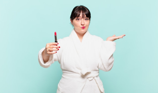 Young woman wearing bathrobe feeling puzzled and confused, doubting, weighting or choosing different options with funny expression