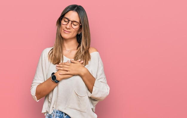 Young woman wearing casual clothes and glasses smiling with hands on chest with closed eyes and grateful gesture on face health concept