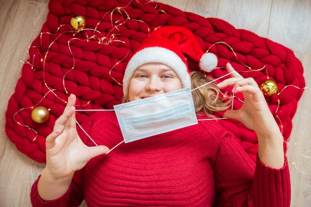 Young woman wearing Christmas hat takes off or puts on a protective mask. Coronavirus and Christmas concept