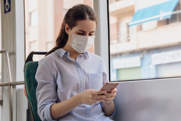 Young woman wearing a face mask and chatting on the phone while traveling by public transport