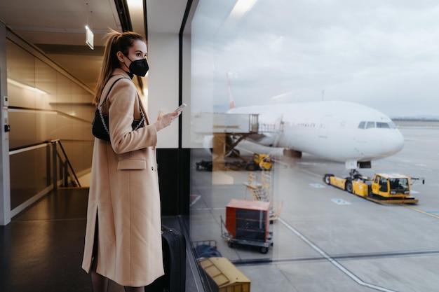 Young woman wearing a face mask and holding a mobile phone Waiting at the airport