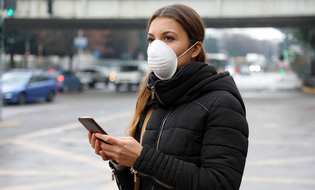 Young Woman Wearing Face Mask Using Smart Phone App in City Street