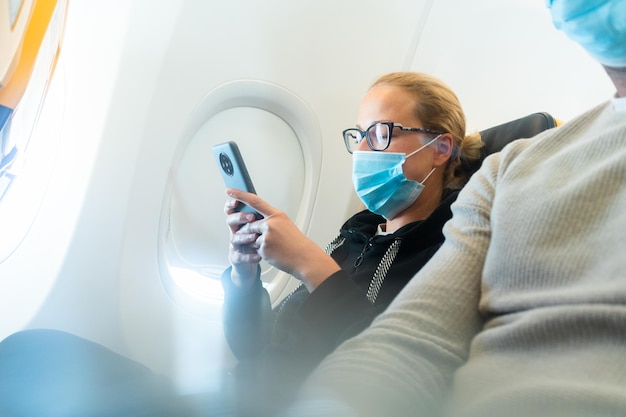 A young woman wearing face mask using smart phone while traveling on airplane