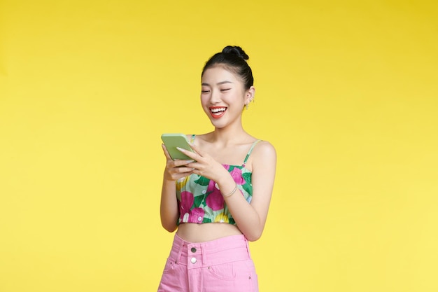 Young woman wearing flower tank top holds mobile phone in hands and rejoices positive news uses modern cellular