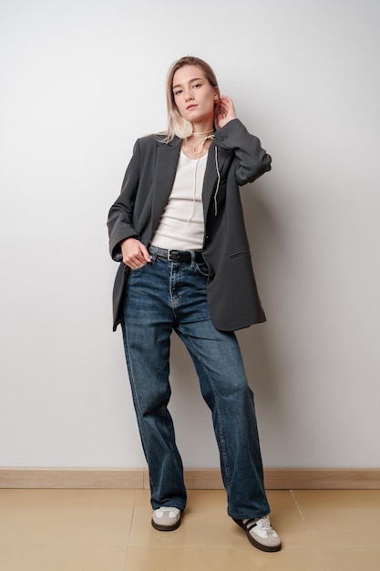 Photo young woman wearing a gray blazer and blue jeans standing against a white wall