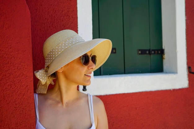 Young woman wearing hat and sunglasses against wall