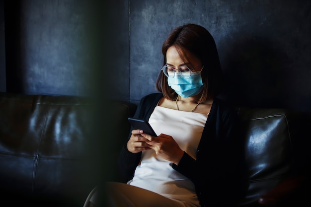 Young woman wearing medical face mask with her phone