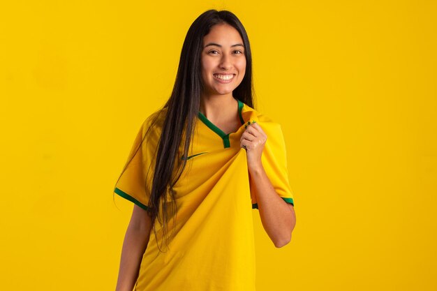 Young woman wearing the official uniform shirt of the Brazilian soccer team at the 2022 Qatar Cup in studio photo Brazilian fan