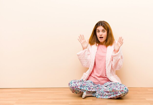 Photo young woman wearing pajamas sitting at home looking shocked and astonished with jaw dropped in surprise when realizing something unbelievable