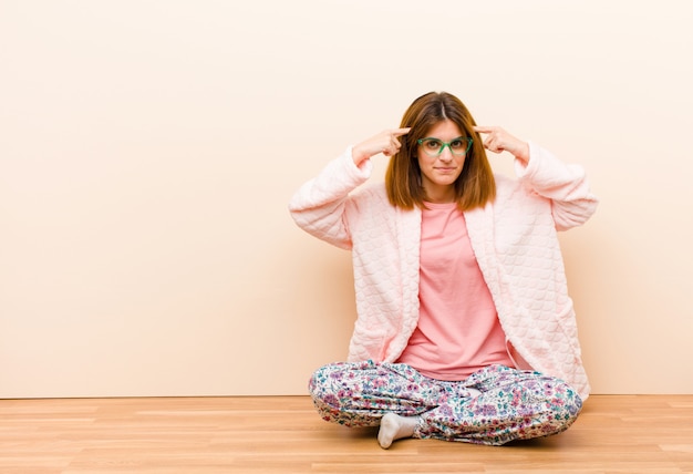 Young woman wearing pajamas sitting at home with a serious and concentrated look, brainstorming and thinking about a challenging problem