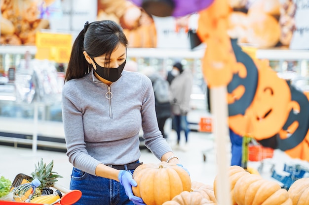 Young woman wearing a protective mask and gloves choosing pumpkins for Halloween