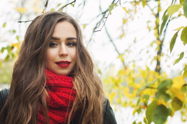 Young woman wearing red woolen scarf outdoor in autumn park