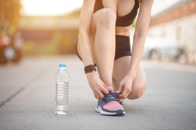 A young woman wearing a running shoe on the road and a water bottle for her