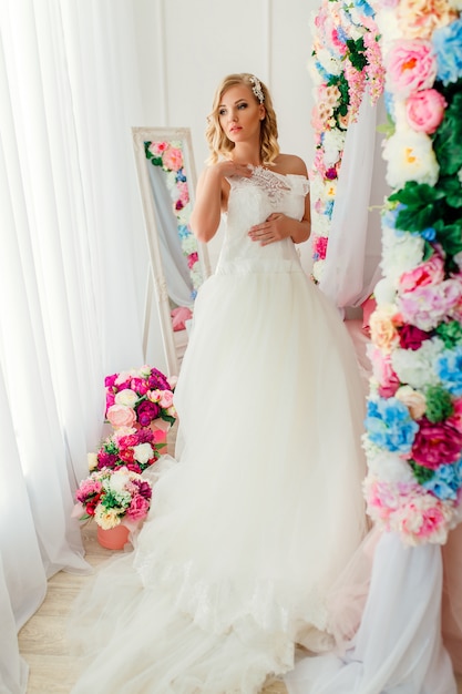 Young woman wearing wedding dress posing in room decorated with flowers