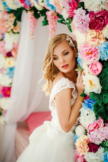 Young woman wearing wedding dress posing in room decorated with flowers