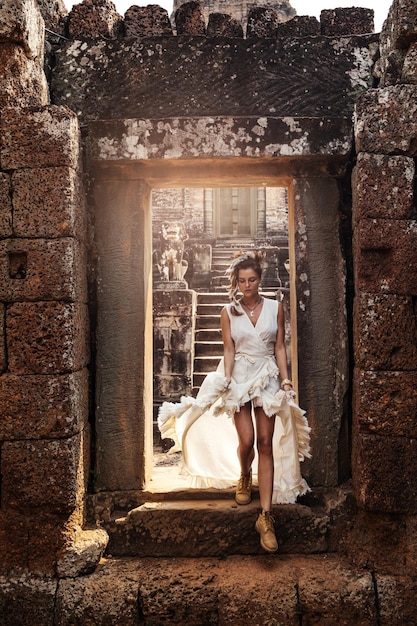 Young woman wearing white robe dress in ancient Khmer ruins Angkor Wat