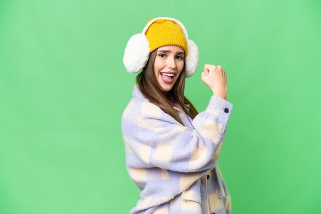 Young woman wearing winter muffs over isolated chroma key background doing strong gesture