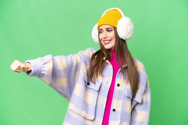 Young woman wearing winter muffs over isolated chroma key background giving a thumbs up gesture