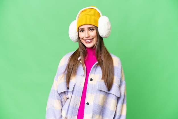 Young woman wearing winter muffs over isolated chroma key background laughing