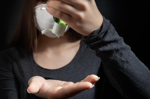 Young woman in a white antibacterial medical mask smears her hands with antiseptic gel