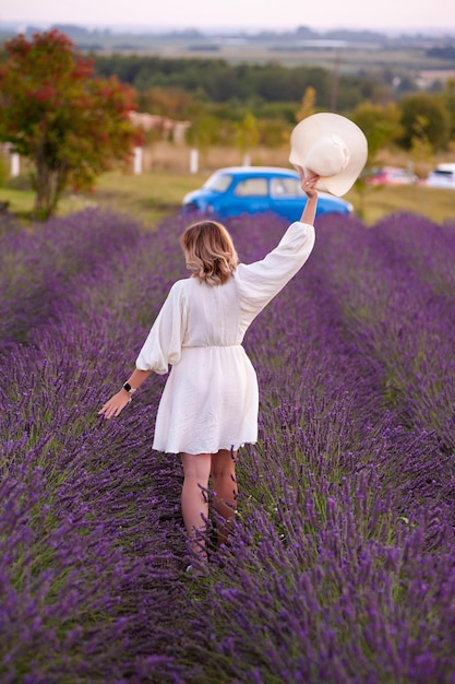 Young woman in a white dress and straw hat running in a lavender field