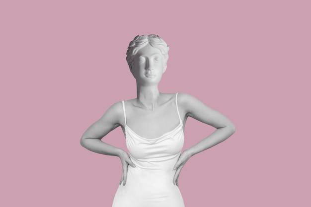 Young woman in white elegant dress headed by antique female statue isolated on a pink background