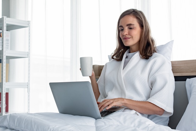 Young woman in white pijamas with white holding a cup of coffee and drink