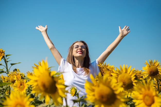 Young woman in a white t-shirt and glasses with raised up hands on a sunflower field