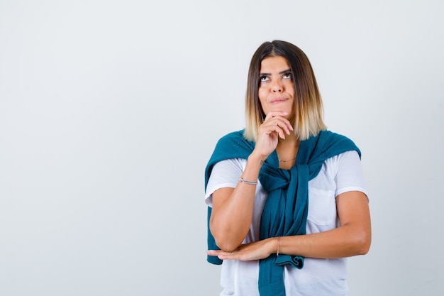 Young woman in white t-shirt with hand on chin and looking dreamy , front view.