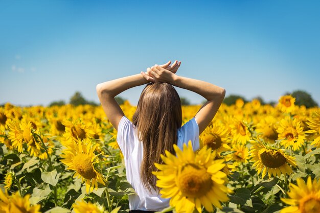 Young woman in white t-shirt with raised hands on a sunflower field on a summer sunny day.