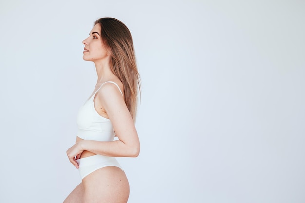 Young Woman White Underwear Standing Sideways On White Background Looking Up Arms Bent Lock