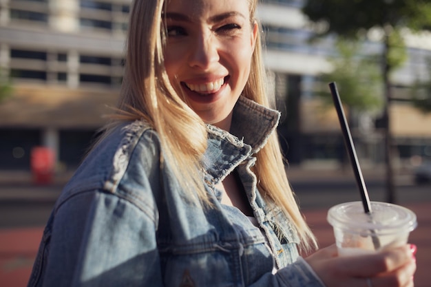 Photo young woman winking while holding disposable cup in city