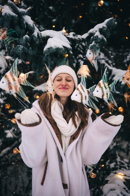 Photo young woman in winter attire surrounded by decorative fish and snow on a festive evening