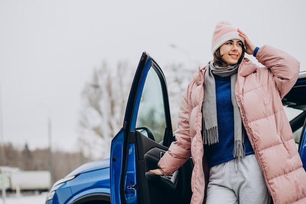 Young woman in winter jacket feeling happy about her new blue car