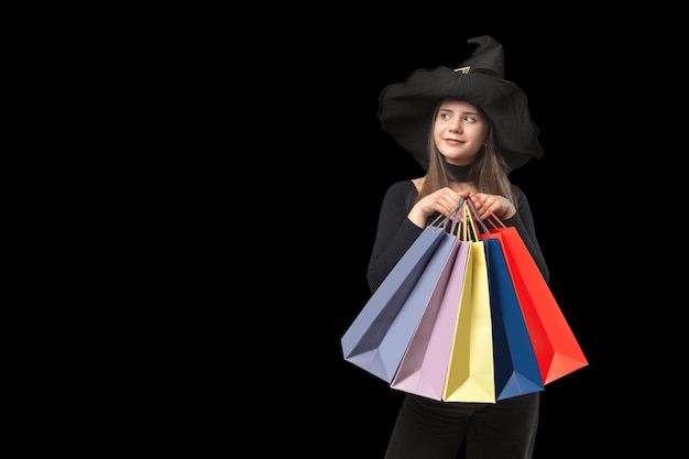 Young woman in witchs hat holds multicolored shopping bags Copy space Black Friday Concept Isolation against black background