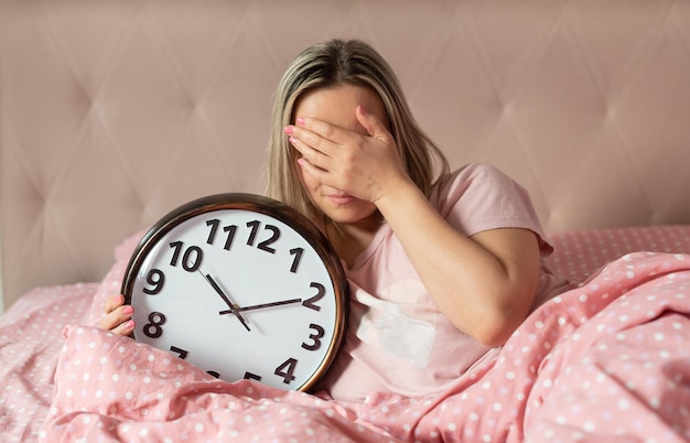 Young woman with alarmclock on the bed at the morning Waking up on an alarm clock Good morning Healthy sleep The biological clock Circadian rhythms