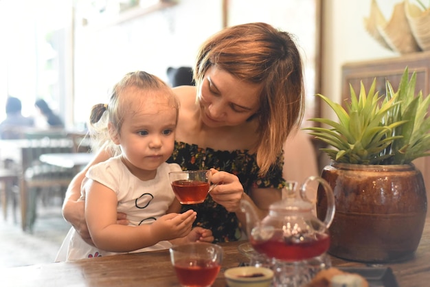 Young woman with a baby girl drinking tea from a tea pot in a coffee shop