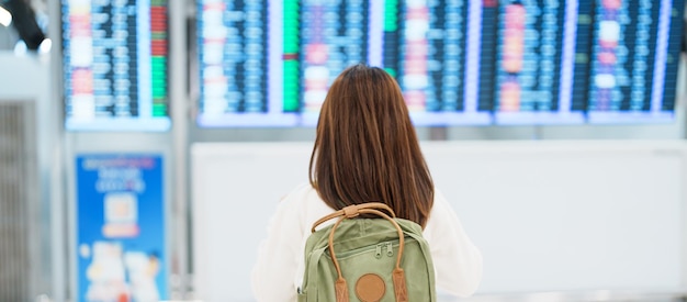 Young woman with backpack looking at the flight time information board in international airport before check in Travel Vacation trip and Transport concept