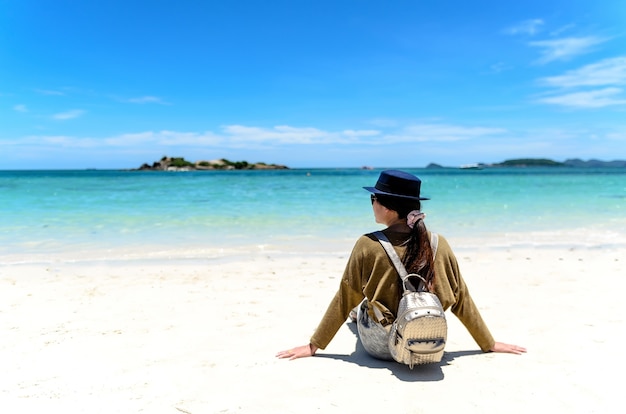 Young woman with backpack sitting on lonely beach and looking into sea.