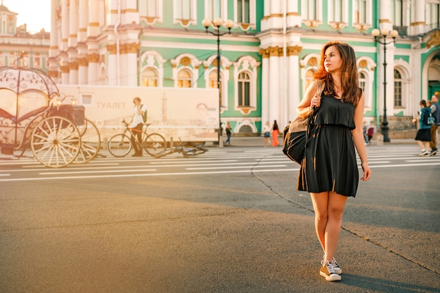 A young woman with a backpack stands in front of the Winter Palace in St. Petersburg