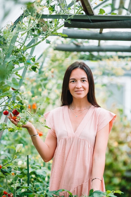 Young woman with basket of greenery and vegetables in the greenhouse. Harvesting time