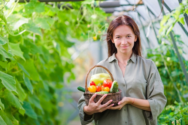 Young woman with basket of greenery and vegetables in the greenhouse. Harvesting time