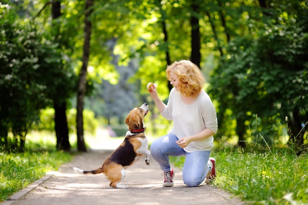 Young woman with Beagle dog in the summer park. Obedient pet with his owner practicing jump command