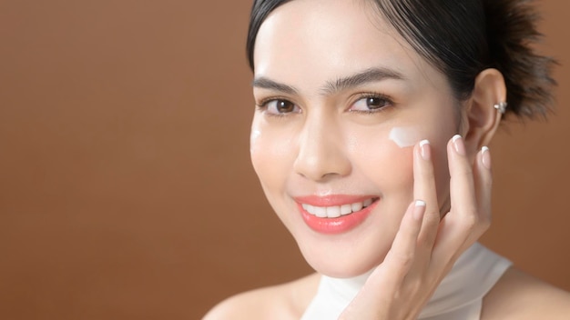 A young woman with beautiful face is holding cream using cream of her face beauty skin care concept