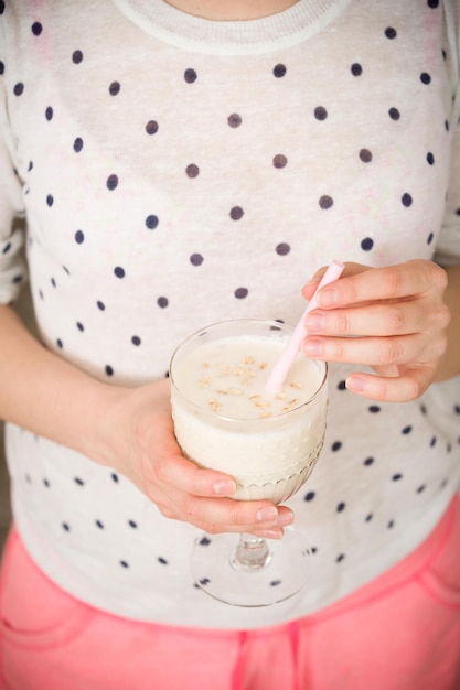 Young woman with a big glass of healthy smoothie served with a straw and oats