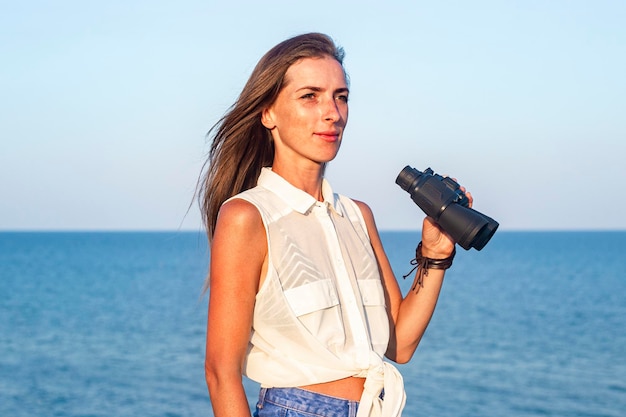 Young woman with binoculars on the cliff against the background of the sea