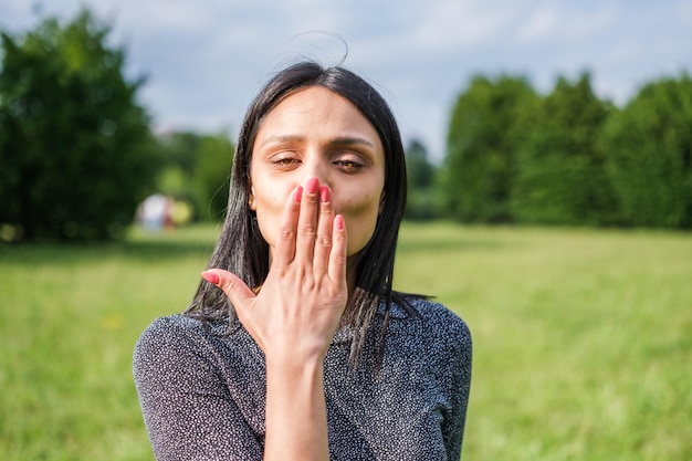 Young woman with black hair sending a greeting through a kiss outdoors