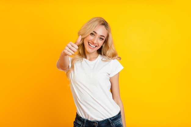 Photo a young woman with blonde hair smiles and gives a thumbs up gesture while wearing a white shirt and