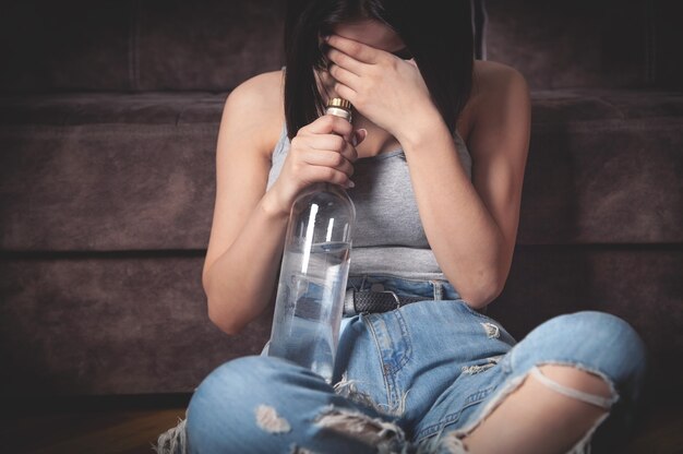 Photo young woman with a bottle of vodka at home.