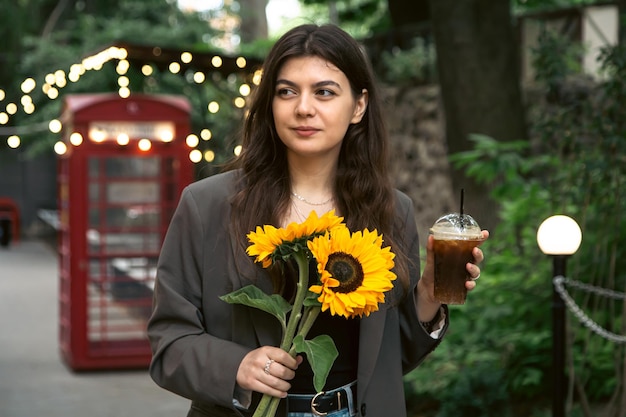 A young woman with a bouquet of sunflowers and a cold coffee drink in the city